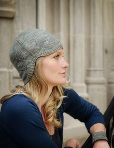 a woman wearing a knitted hat sitting next to a building and looking off into the distance