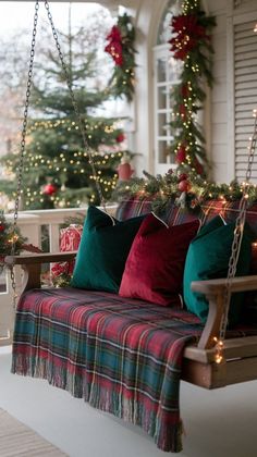 a porch swing with christmas decorations and lights on the back wall, along with plaid throw pillows