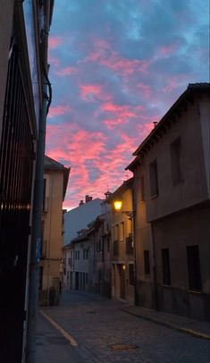 the sun is setting over an alleyway with old buildings and cobblestone streets