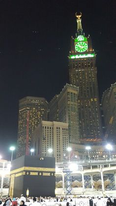 a large clock tower in the middle of a city at night with people walking around