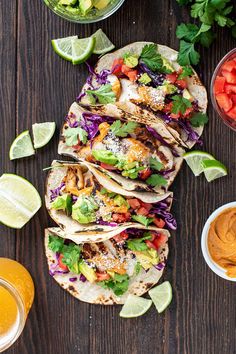 several tacos are lined up on a table with salsa, limes and avocado