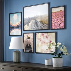 a blue wall with pictures on it and a lamp next to the dresser in front