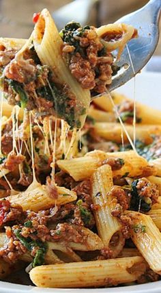 a spoonful of pasta with meat and spinach on it is being lifted from a white plate