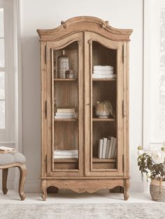 an old wooden cabinet with glass doors and shelves in the corner next to a chair