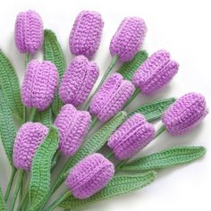 purple crocheted flowers with green leaves on white background