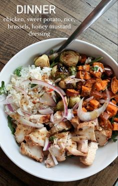 a white bowl filled with chicken, rice and veggies on top of a wooden table