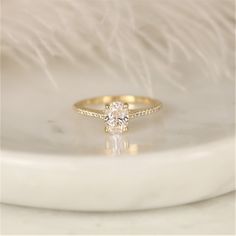 a diamond ring sitting on top of a white marble slab with feathers in the background