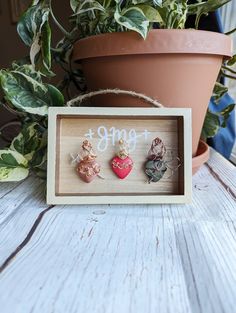 two small hearts are in a wooden frame on a table next to a potted plant