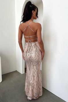 a woman in a long dress standing against a wall with her back to the camera