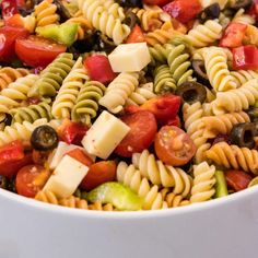 a pasta salad with olives, tomatoes, and other vegetables in a white bowl