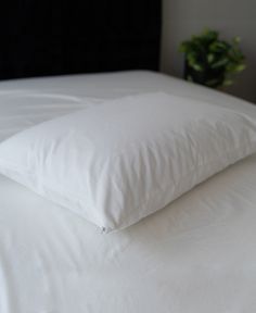 a white pillow sitting on top of a bed next to a night stand with a plant