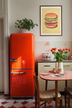 an orange refrigerator in a kitchen next to a table with flowers and potted plants