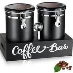 two black coffee canisters sitting on top of a wooden box with the word coffee bar painted on it