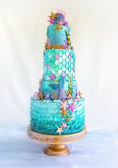 a three tiered cake with blue icing and stars on the top is sitting on a gold pedestal