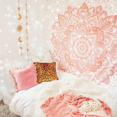 a white bed topped with pink pillows and blankets next to a wall covered in lights