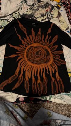 a black shirt with an orange sun on it sitting on top of a bed covered in sheets