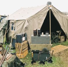 an army tent with many items in front of it on the grass and dirt ground