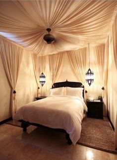 a bed sitting under a white canopy in a bedroom next to two lamps on either side of the bed