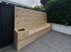 a wooden bench sitting on top of a cement floor next to a fence and shrubbery