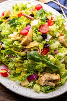 a salad with chicken, lettuce and tomatoes on a white plate sitting on a wooden table