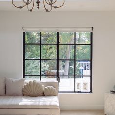 a white couch sitting under a window in a living room next to a chandelier