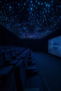 an empty theater with rows of seats in front of a projector screen and stars on the ceiling