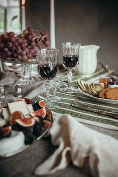 a table topped with plates of food and glasses of wine next to a bowl of fruit