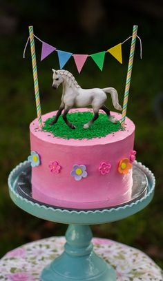 there is a pink cake with a horse on top and bunting around the edges