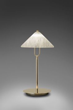 a table lamp with a white shade on it's side and a gold base