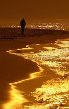 a man standing on top of a sandy beach next to the ocean at night time