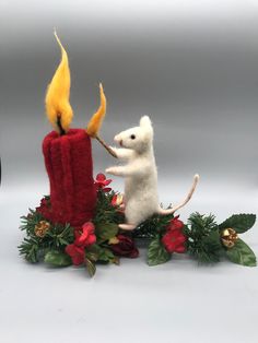 a small white mouse sitting next to a red candle with a yellow flame on it