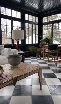 a living room with black and white checkered flooring, large windows, wooden furniture, and potted plants