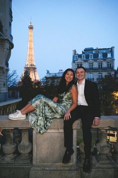 a man and woman are sitting on a ledge in front of the eiffel tower