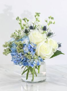 a bouquet of white and blue flowers in a glass vase on a marble countertop