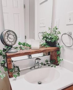 a bathroom sink with plants on the counter and a mirror above it that has a clock