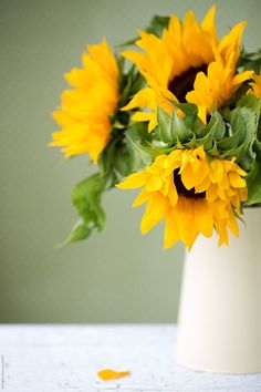 a white vase filled with yellow sunflowers on top of a table