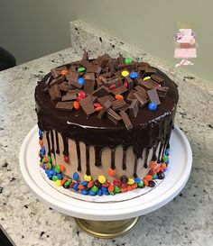 a cake with chocolate frosting and candy toppings on a white plate sitting on a counter