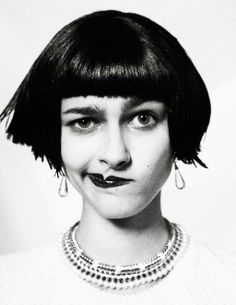 a black and white photo of a woman with short hair, wearing a necklace and earrings