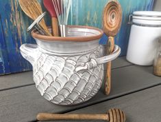 a ceramic container with wooden spoons and whisk in it on a table