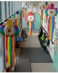 there are many colorful kites hanging on the wall in this school hallway that is decorated with clown faces and rainbow colors