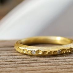 a close up of a gold wedding ring on a wooden surface with a white object in the background