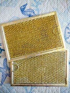 two gold colored metal boxes sitting on top of a blue and white table cloth with sea shells