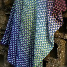 a blue, green and pink blanket hanging on a brick wall next to a pile of bricks