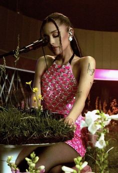 a woman in a pink dress is sitting on a stool with flowers and plants around her