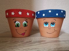 two clay pots with faces painted on them sitting on a wooden table next to a wall