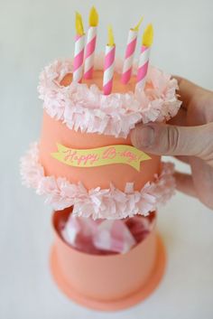 someone is holding a cupcake with candles in it and pink flowers on the bottom