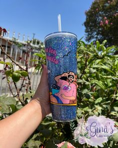 a hand holding up a blue glittered cup with an image of princess aurora on it