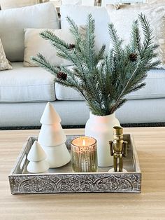 a tray with candles and pine cones in it on a table next to a couch