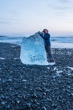 a man standing next to an ice block on the beach