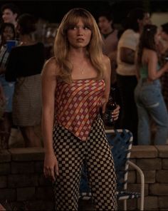 a woman standing in front of a crowd wearing checkered pants and an orange top